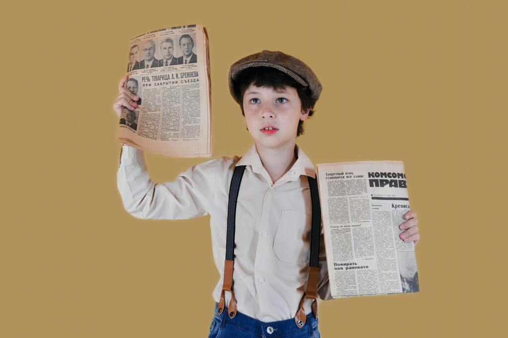 A child dressed in retro attire holding historical Russian newspapers against a yellow background.